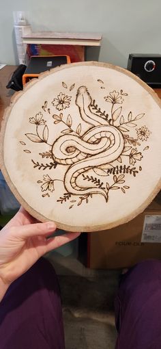 a person holding up a wooden plate with a snake on it