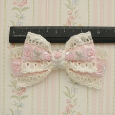 a pink and white lace bow with flowers on the side next to a ruler that is measuring