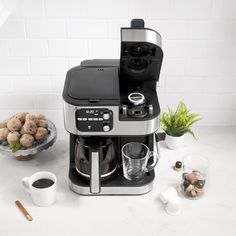 a coffee maker sitting on top of a counter next to a bowl of food and cups