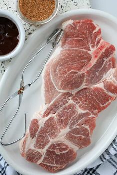 two pieces of raw meat sit on a white plate next to some spices and spoons