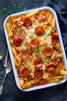 a casserole dish with pepperoni, cheese and french fries in it next to silverware