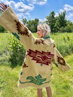 a woman is standing in the grass with her arms out and she's wearing a sweater