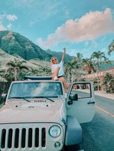 a woman sitting on the hood of a white jeep in front of mountains and palm trees