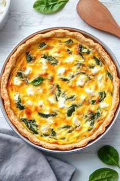 a quiche with spinach and cheese in a pie pan on a white table