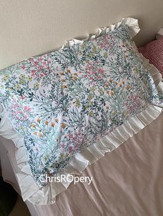 a white bed topped with a floral comforter next to a red and white pillow