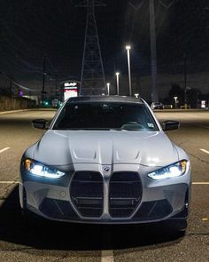 the front end of a silver sports car parked in a parking lot at night with its lights on