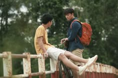 two young men standing next to each other on a bridge