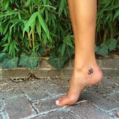 a person's foot with a small tattoo on the side of their leg, in front of some bushes