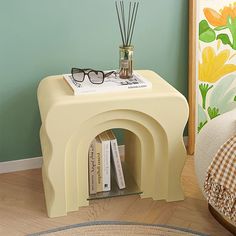 a white table with a book and glasses on it next to a flowered wall