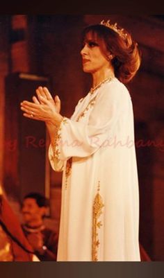 a woman in a white dress and crown standing with her hands folded up while wearing a tiara