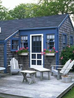 a deck with chairs, table and potted plants on it in front of a blue house