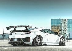 a white sports car parked in a parking lot next to tall buildings and skyscrapers