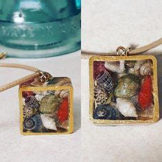 two square pendants with seashells on them sitting next to a blue bottle