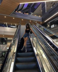 a woman is riding down an escalator with her luggage