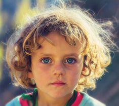 a close up of a child with blue eyes wearing a green and red shirt looking at the camera