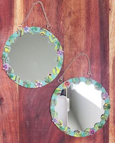 two mirrors hanging from chains on a wooden table next to a mirror with flowers painted on it