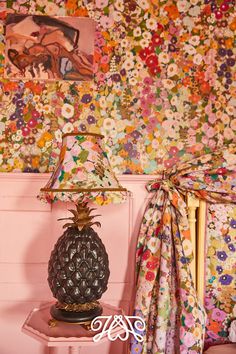 a pineapple lamp sitting on top of a pink table next to a wall covered in flowers