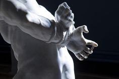 a white statue holding his hands together in front of a dark background with light coming through it