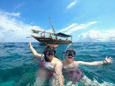 two people in the water with snorkels on their heads, and a boat in the background