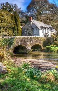 an old stone bridge over a river with a house in the background on a sunny day