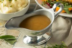 a gravy in a silver gravy boat next to a plate of mashed potatoes