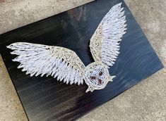 a metal sculpture with white wings on top of a wooden board in the shape of an owl