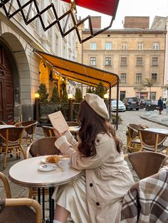 a woman sitting at a table reading a book in an outdoor cafe with tables and chairs