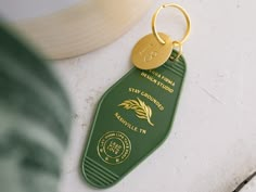 a green keychain with a gold tag on it sitting next to a plant