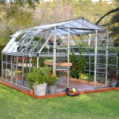 a small greenhouse in the middle of a yard with potted plants and other items