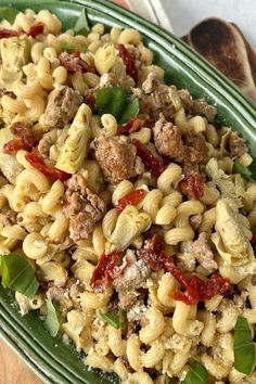 a green plate filled with pasta and meat on top of a wooden table next to bread