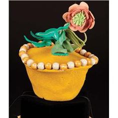 a yellow hat with flowers and beads on the top is sitting on a black surface