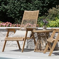 two wicker chairs sitting next to a table with a vase on it and flowers in the background