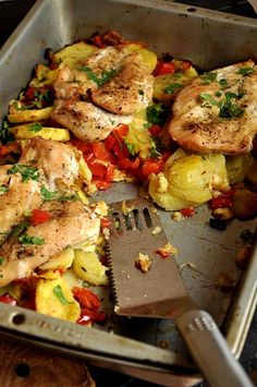 a pan filled with chicken and vegetables next to a spatula