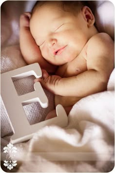 a baby is sleeping next to the letter e with its eyes closed and it's head propped up