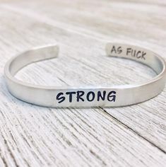 a silver bracelet with the words strong as flickk written on it, sitting on a wooden surface