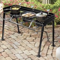 an outdoor grill with pots and pans on it's burners, sitting on a brick patio