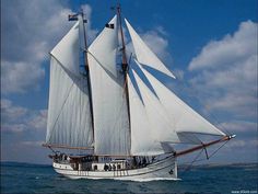 a sailboat with white sails sailing in the ocean under a blue sky filled with clouds