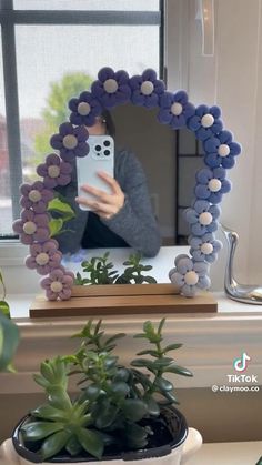 a person holding up a mirror made out of beads and plastic balls with a cell phone in the middle