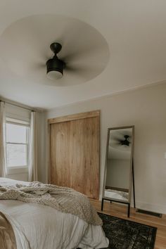 a bedroom with a bed, dresser and mirror in it's corner next to a window