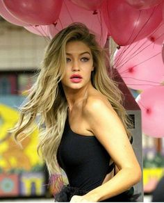 a woman in a black dress with pink balloons on her head and long blonde hair