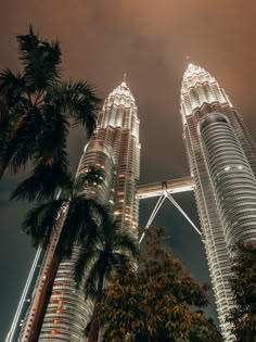 two very tall buildings towering into the sky at night with palm trees in foreground