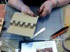 a woman is making a house out of cardboard with scissors and glue on the table