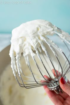 a hand holding a whisk with whipped cream on it in a mixing bowl