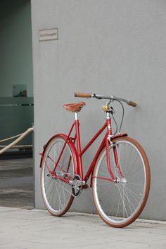 a red bike parked next to a gray wall and roped off area in front of it