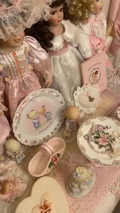 many dolls and plates on a table with pink cloths, hats, and other items