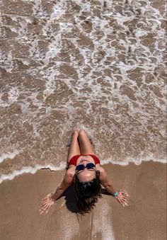 a woman laying on top of a sandy beach next to the ocean with her feet in the water