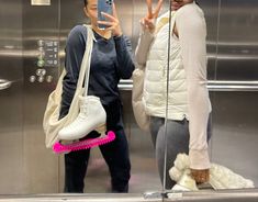 two people standing in front of an elevator taking a selfie with their cell phone