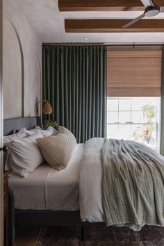 a bed sitting in a bedroom next to a window covered in green curtains and pillows