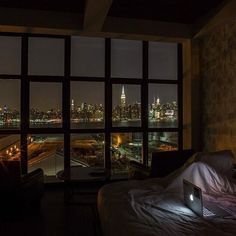 a laptop computer sitting on top of a bed in front of a window overlooking the city