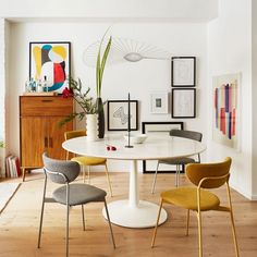 a white table with yellow chairs and pictures on the wall behind it in a living room